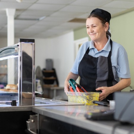 A female member of our catering team holding a food container, whilst stood behind a serving counter.