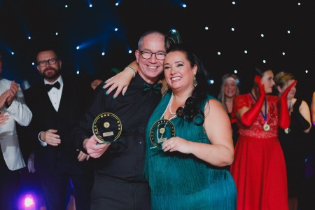 Diane wraps her arm around Dave as they hold their awards after being named audience champion at the dancing event. Dave is wearing a black suit and Diane is wearing a green dresss