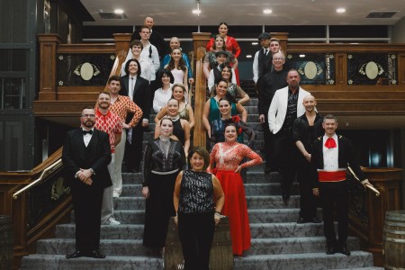 Participants in the Liverpool Women's Hospital Strictly 2024 event are standing on the staircase at the Titanic Hotel dressed in their dancing outfits